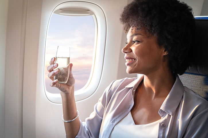 Lady in window seat on plane drinking water