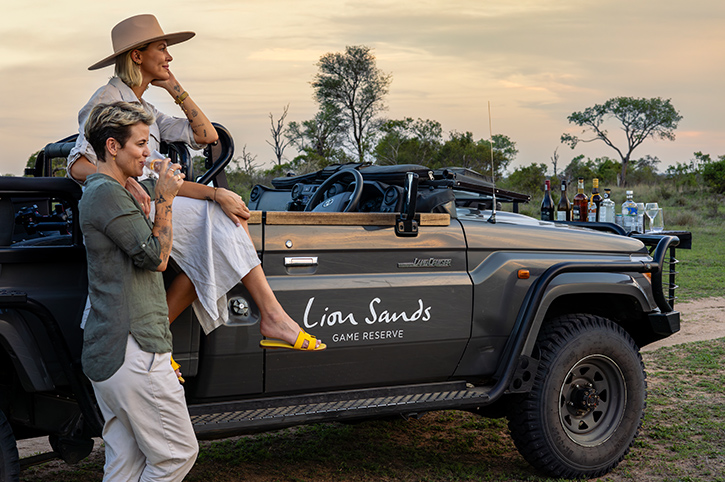 2 ladies enjoying sundowners by a safari Vehcile, Lion Sands, South Africa